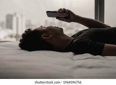 Asian Man Feels Sad On Bed Looking And Focus On Smartphone. Internet Social Media Addiction And Mental Health Concept.