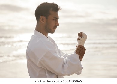 Asian man, fighter and bandage wrapping fist at beach for martial arts, training or exercise to prepare for karate. Calm, warrior or zen judo master at sea ready for tournament, practice or workout - Powered by Shutterstock