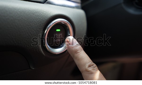 Asian man finger pushing car engine start and\
stop button.