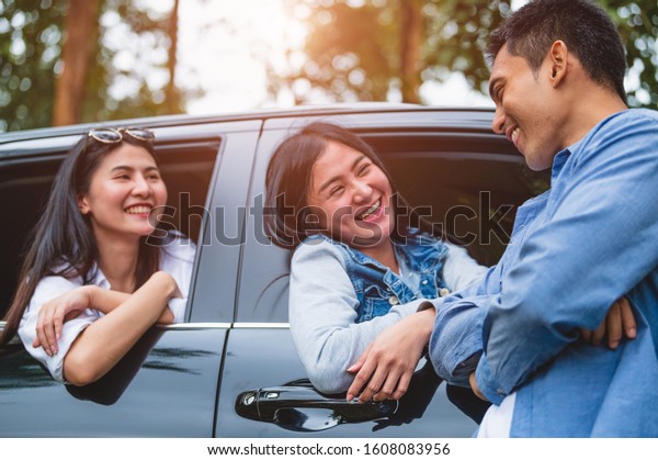 Asian man flirting women in car during travel in\
forest. Boy talking to girls for meeting. People lifestyles and\
weekend tour concept. Summer and nature theme. Mountain camping\
people group in holiday
