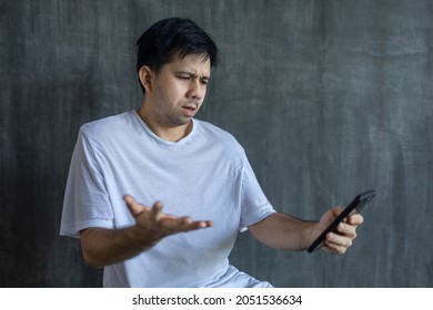 Asian Man Frowns At His Smartphone In An Upset Mood, Technology Intelligence, Internet Outage