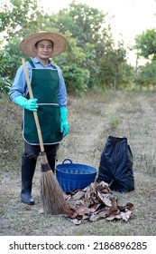  Asian Man Gardener Holds Bloom, Basket And Black Garbage Bag  To Get Rid Dry Leaves  In Garden. Concept : Cleaning Garden. Forest Fire Prevention. Use Dry Leaves To Make Compost. Full Body Image.