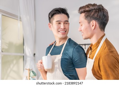 Asian Man Gay Family In Apron Standing And Drink Coffee For Breakfast. Attractive Romantic Male Lgbtq Couple Celebrate Anniversary Or Spending Time On Vacation In Kitchen. Homosexual-LGBTQ Concept.
