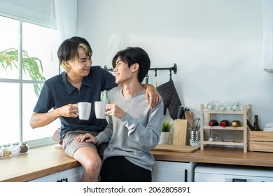 Asian Man Gay Family Sitting On Counter, Drink Coffee For Breakfast. Attractive Romantic Male Lgbtq Couple Celebrate Anniversary, Spend Time Have Dinner In Kitchen In House. Homosexual-LGBTQ Concept.