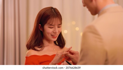 asian man giving propose for marriage to his girlfriend with ring and wear it in living at night home