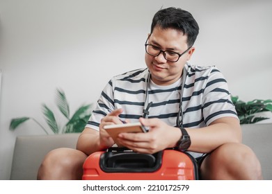Asian Man Glasses Is Preparing Clothes In Suitcases. He's Choosing Clothes, Travel Documents, The Itinerary For A Solo Trip, And Check The Checklist. Travel, Holiday And Vacation Concept.