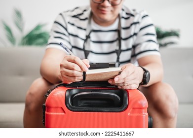 Asian man glasses is preparing clothes in suitcases. He's choosing clothes, travel documents, the itinerary for a solo trip, and check the checklist. Travel, holiday and vacation concept.