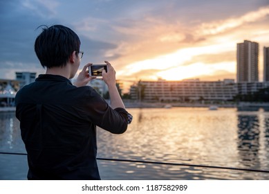 Asian man with glasses using smartphone camera taking photo during the sunset in the city. Urban lifestyle with mobile phone technology concept - Powered by Shutterstock