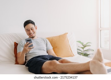 Asian Man Happy With The Mobile Application While Relax On His Sofa.