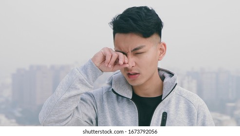 asian man has allergy and has itchy eyes standing in the city
