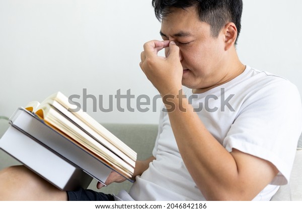 Asian man has problems with eye strain,vision\
disorders while reading books for too long,dry eyes and irritated\
pain,massaging nose bridge with fingers and eye socket massage to\
relax and relieve pain