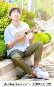 Asian man with hat playing guitar ukulele at outdoor