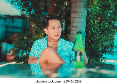 Asian Man In A Hawaiian Luau Polo Shirt In A Fashionable Summer Set Taking A Selfie With Phone With His Reflection On Table.