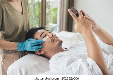 Asian Man Healthy Facial Face Care With Beautician Use Applying Eye Mask For Under Eye Anti Wrinkle In Spa Salon. Young Male Happy In Salon.