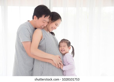 Asian Man And His Daughter Hugging Pregnant Wife And Smile Together