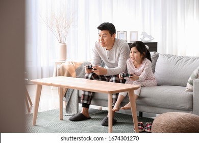 Asian Man And His Little Daughter Playing Video Game At Home