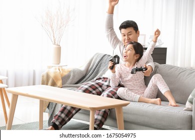 Asian Man And His Little Daughter Playing Video Game At Home