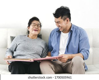 Asian Man And His Mother Looking At Photo Album Together While Staying At Home.