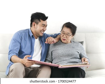 Asian Man And His Mother Looking At Photo Album Together While Staying At Home.