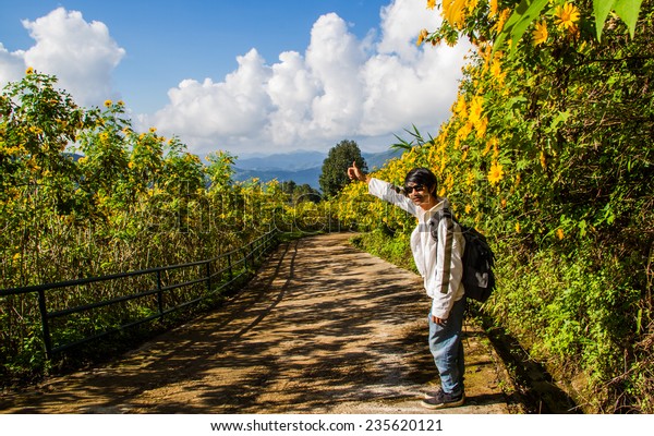 Asian man\
hitchhiking  on the flower field\
road.