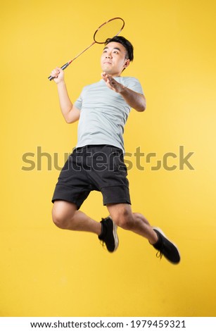 Asian man holding badminton racket and jumping on yellow background

