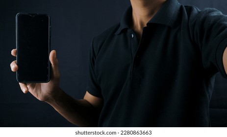 Asian man holding big smartphone with blank screen in hand, showing close to camera and pointing at device. Gadget with empty free space for mock up, banner - Shutterstock ID 2280863663