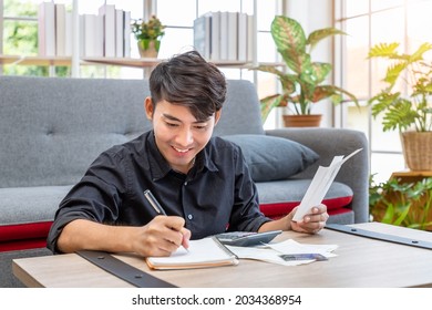 Asian Man Holding Bill And Calculating Credit Card Expenses Receipt Using Calculator Sitting In Living Room At Home, Personal Finance Concept