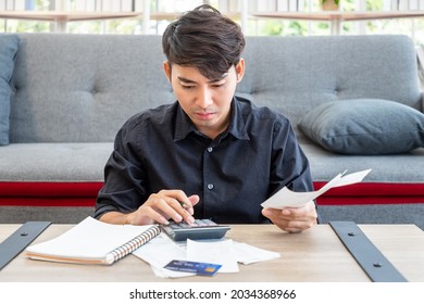 Asian Man Holding Bill And Calculating Credit Card Expenses Receipt Using Calculator Sitting In Living Room At Home, Personal Finance Concept