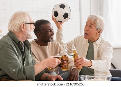 Asian Man Holding Football Near Multiethnic Friends With Beer At Home