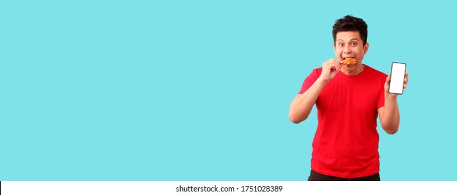 Asian Man Holding Mobile Phone Giving Food Order Fried Chicken Isolated On Blue Background In Studio With Copy Space.