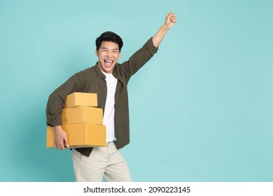 Asian man holding package parcel box and hands up raised arms isolated on green background, Delivery courier and shipping service concept