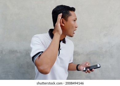 Asian Man Holding A Phone And Hand To Ear Gesture Isolated On Grey Background.