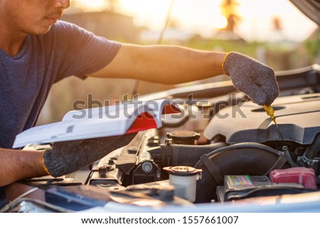 Asian man holding and reading the car user manual or user instruction to checking or fixing engine of modern car. Car maintenance or service before driving concept
