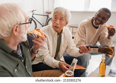 Asian Man Holding Remote Controller Near Interracial Friends With Beer And Pizza At Home