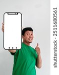 Asian man holding smartphone with empty blank screen and thumb up expression ok sign. good. Indonesian man wearing green t-shirt with hand forming ok sign and holding phone. smiling happy man.