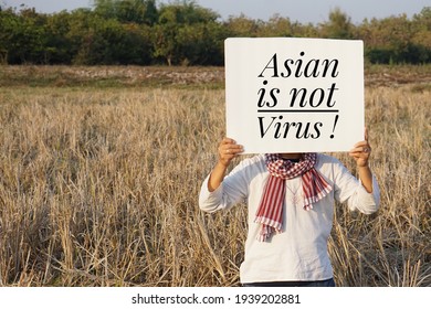 Asian man holds paper sign with English word "Asian is not Virus" at rural field. Concept calling for global sympathy to stop hating or mistaking Asians for the cause of spreading of Covid-19. 