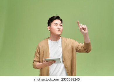 An Asian man holds the tablet in his hand, raises his hand, points to the air and smiles happily  - Powered by Shutterstock