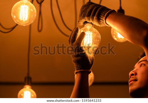 Asian man / house owner cleaning or\
changing vintage light bulb. House maintenance\
concept