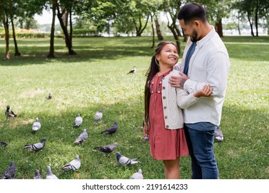 Asian Man Hugging Preteen Daughter Near Doves In Park