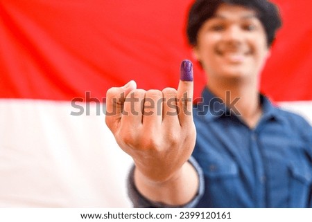Asian man with Indonesia flag on the background showing little finger with blue ink patches as a mark from Indonesia election, selective focus