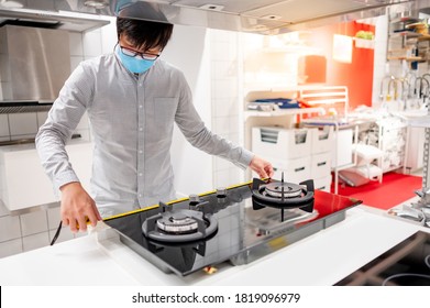 Asian Man Interior Designer Wearing Face Mask Using Tape Measure On Gas Stove On Counter In Kitchen Showroom. Shopping Appliance For Domestic Kitchen. Home Improvement Concept