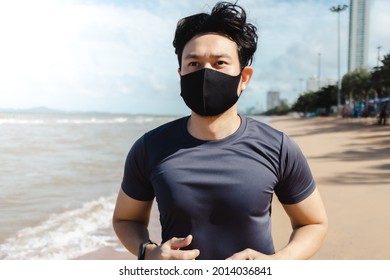 Asian Man Jogging On The Beach With Mask In Summer Morning.