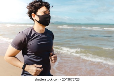 Asian Man Jogging On The Beach With Mask In Summer Morning.