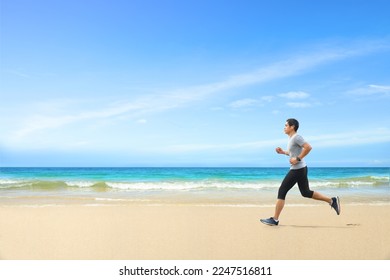 Asian man jogging  on tropical sandy beach with blue sea and clear sky background. - Powered by Shutterstock