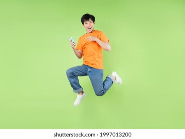 Asian Man Jumping And Holding Smartphone , Isolated On Green