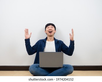 Asian Man With Laptop Cheerful And Feeling Happy Looking Up At Space Sitting On The Floor