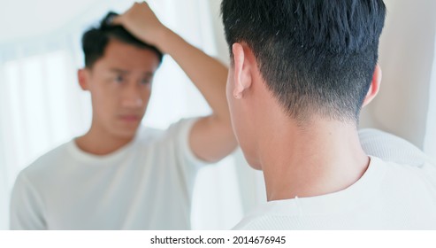 asian man look at his face in mirror and check hair and hairline