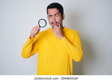 Asian man looking something using magnifying glass with curious face expression