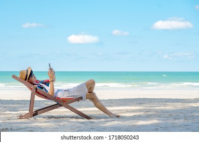 Asian man lying on beach chair using smartphone chatting or online shopping during travel at the beach on summer holiday vacation. People enjoy outdoor lifestyle with gadget device and online network. - Powered by Shutterstock