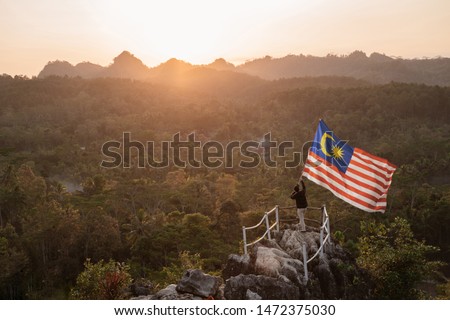 asian man with malaysian flag of malaysia on top of the mountain